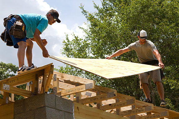 carpenters placing plywood on a roof