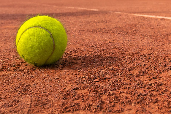 yellow tennis ball on dirt tennis court